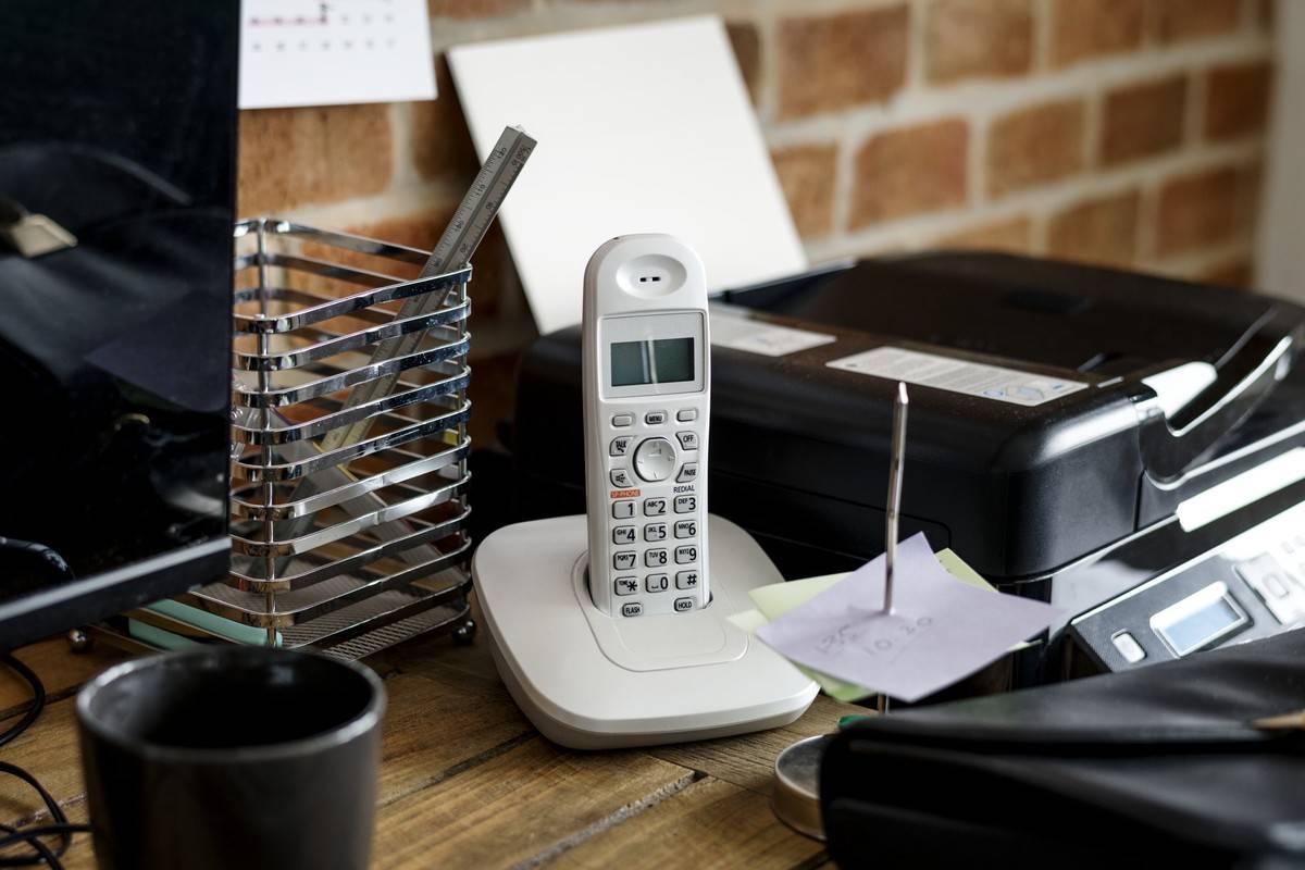 Téléphone sans fil posé sur sa base, sur un bureau d'entreprise, à côté d'une imprimante