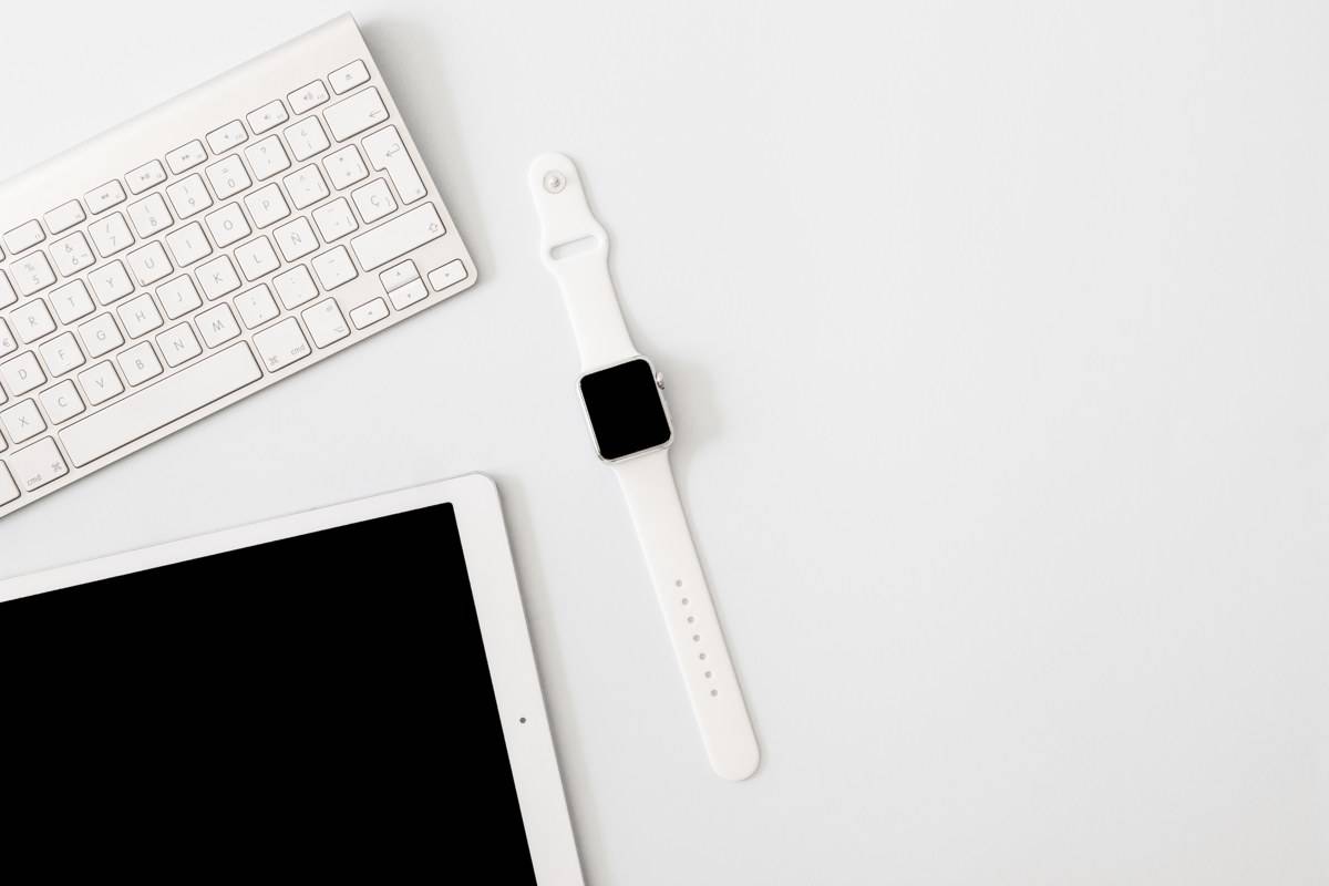 Montre connectée blanche posée à côté d'un clavier et d'une tablette sur un bureau