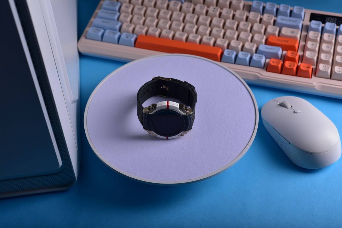 Montre connectée noire posée sur un socle près d'un clavier et d'une souris sans fil