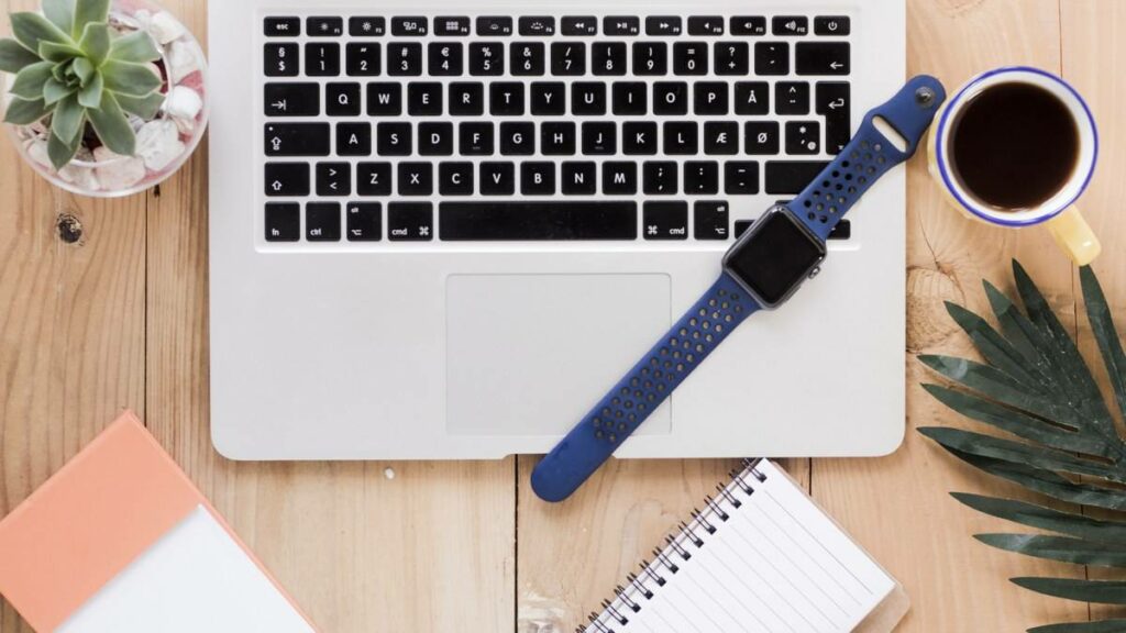 Montre connectée posée sur le clavier d'un ordinateur portable, à côté d'un café et d'une plante