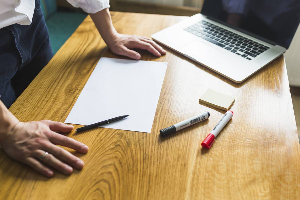 Main posée sur une feuille blanche sur un bureau en bois